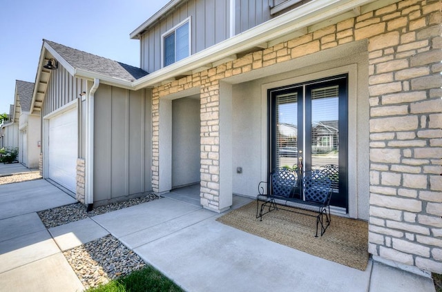 property entrance with an attached garage, roof with shingles, and board and batten siding