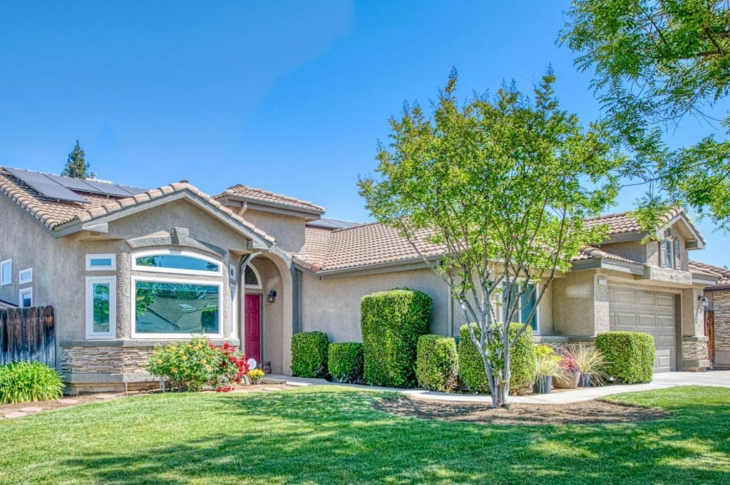 5124 W Bedford Ave, Fresno, CA 93722 - view of front facade featuring roof mounted solar panels, a tiled roof, a front yard, and stucco siding