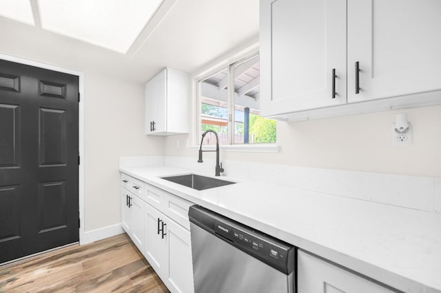 kitchen with stainless steel dishwasher, a sink, light countertops, and light wood-style floors