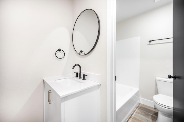 full bathroom with wood finished floors, a bath, vanity, baseboards, and toilet