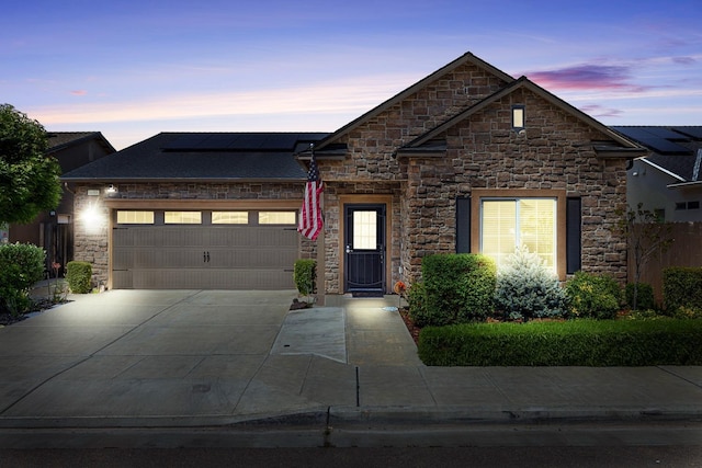 view of front of home featuring driveway, a garage, solar panels, and stone siding