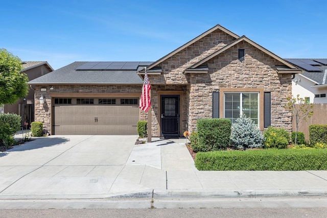 view of front facade featuring stone siding, solar panels, driveway, and an attached garage
