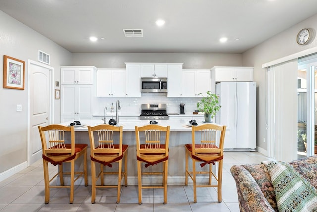kitchen featuring stainless steel appliances, light countertops, backsplash, visible vents, and a center island with sink