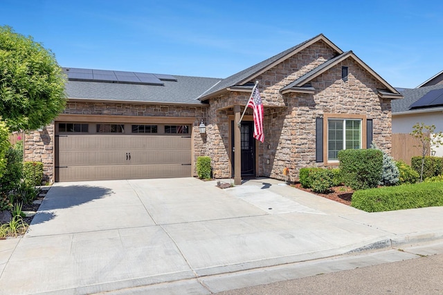 view of front facade with a shingled roof, driveway, stone siding, roof mounted solar panels, and an attached garage
