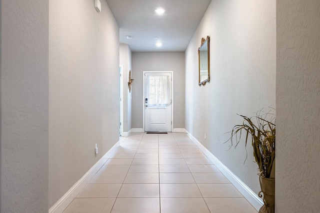 hallway featuring light tile patterned flooring, a textured wall, recessed lighting, and baseboards