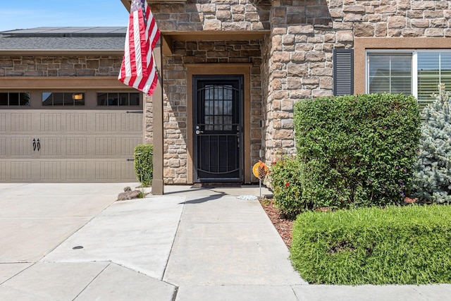 view of exterior entry with driveway, solar panels, and stone siding