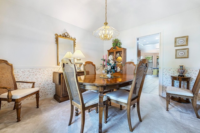 dining space with light colored carpet, wallpapered walls, a notable chandelier, and a wainscoted wall