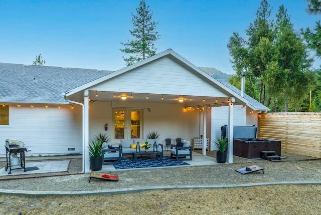rear view of property with fence, a hot tub, a patio, an outdoor hangout area, and roof with shingles