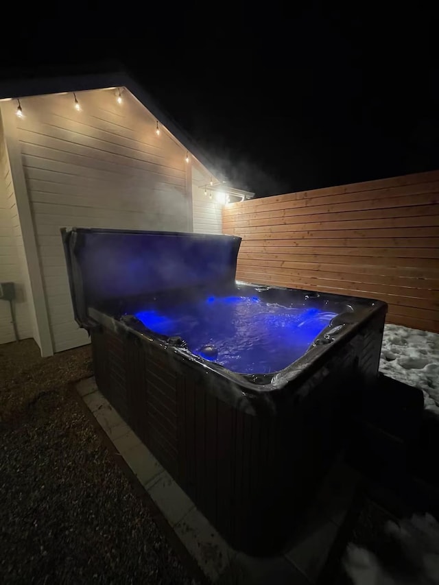 patio at night featuring fence and a hot tub
