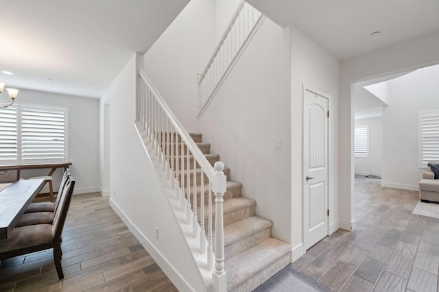 stairs featuring an inviting chandelier, wood finished floors, and baseboards
