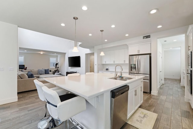 kitchen with white cabinetry, a sink, stainless steel appliances, light countertops, and a kitchen island with sink