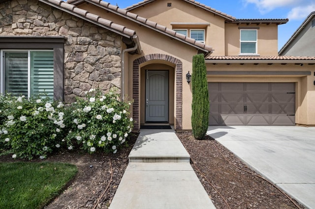 doorway to property with stucco siding, a tiled roof, a garage, stone siding, and concrete driveway