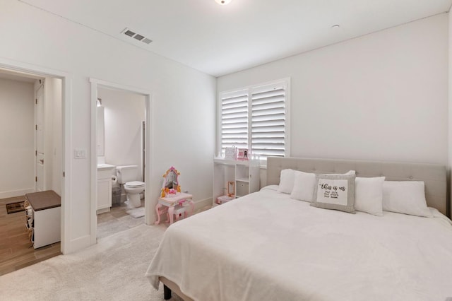 bedroom with baseboards, visible vents, light carpet, and ensuite bath