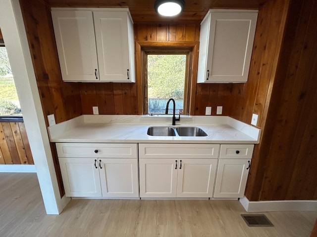 31083 Bear Paw Way, Coarsegold, CA 93614 - kitchen with white cabinetry, a sink, wood walls, visible vents, and light wood-style floors