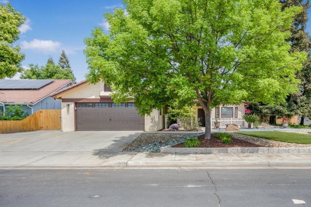 view of property hidden behind natural elements featuring fence, stucco siding, driveway, and an attached garage