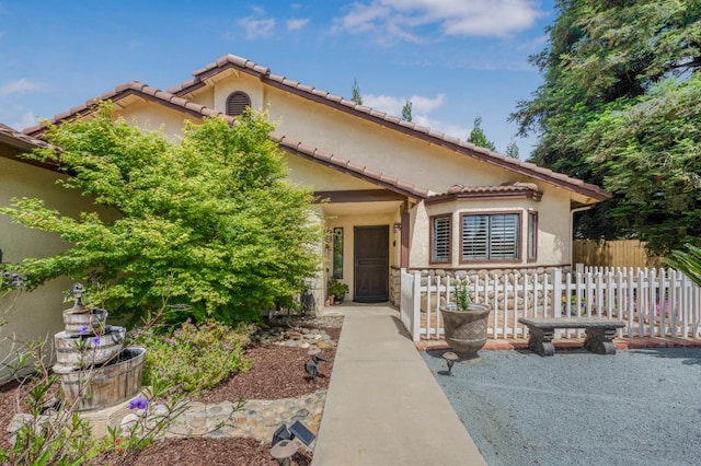 mediterranean / spanish home with stucco siding, a tiled roof, and fence