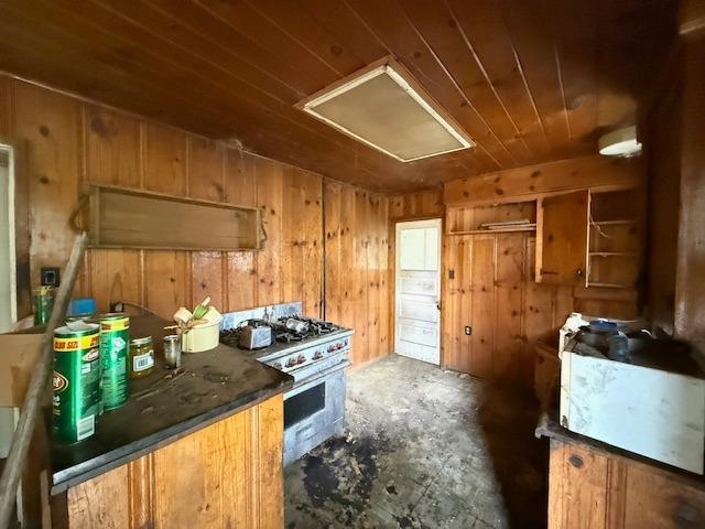 28826 Auberry Rd, Clovis, CA 93619 - kitchen featuring stainless steel range with gas cooktop, wood ceiling, concrete floors, wooden walls, and brown cabinetry