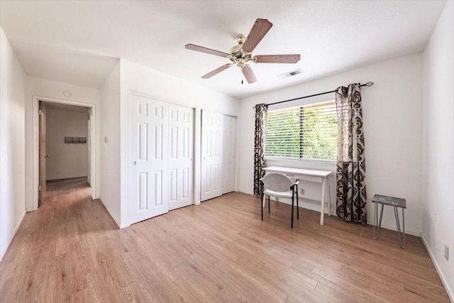 bedroom with two closets, light wood-type flooring, baseboards, visible vents, and a ceiling fan