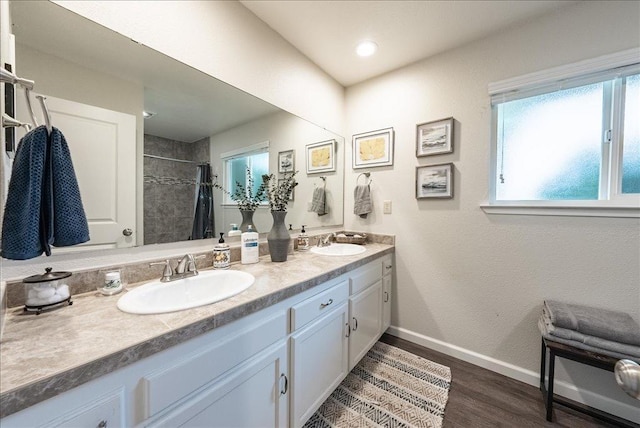 bathroom featuring a sink, a tile shower, double vanity, baseboards, and wood finished floors