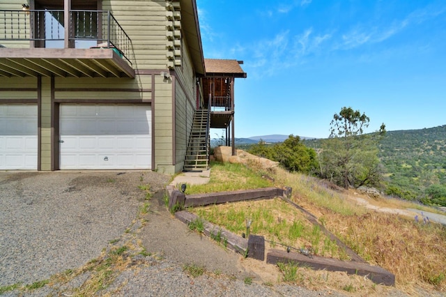 view of side of home featuring driveway, stairs, a balcony, a mountain view, and an attached garage