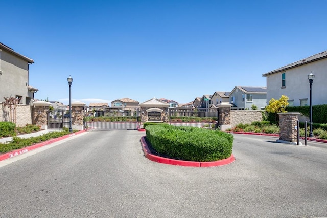 view of street with curbs, a residential view, a gate, a gated entry, and street lights
