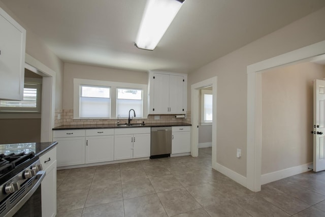 kitchen featuring decorative backsplash, stainless steel appliances, white cabinets, dark countertops, and a sink
