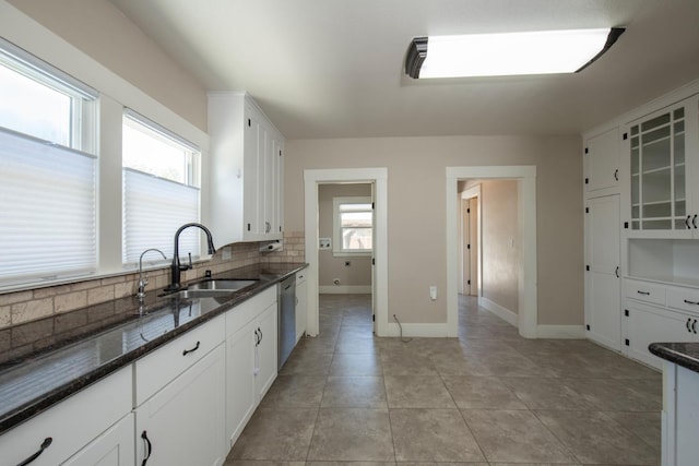 kitchen featuring dark stone countertops, backsplash, dishwasher, a sink, and white cabinetry