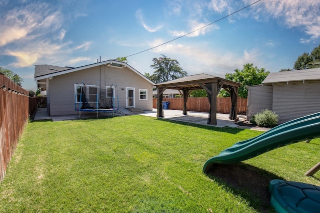 back of house with a trampoline, a fenced backyard, a gazebo, a patio, and a lawn