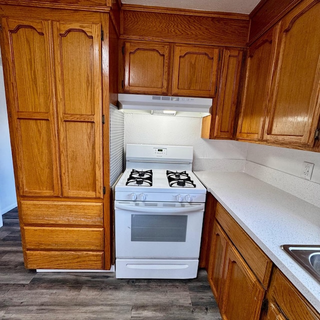 201 Walnut St, Madera, CA 93637 - kitchen with under cabinet range hood, white range with gas stovetop, brown cabinetry, light countertops, and dark wood-type flooring