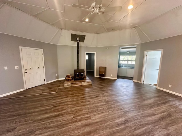 unfurnished living room featuring baseboards, a wood stove, ceiling fan, and lofted ceiling