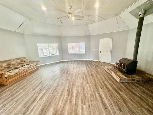 unfurnished living room with a wood stove, ceiling fan, lofted ceiling, baseboards, and wood finished floors