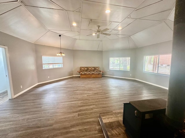 unfurnished living room with vaulted ceiling, ceiling fan with notable chandelier, a wealth of natural light, and dark wood-type flooring