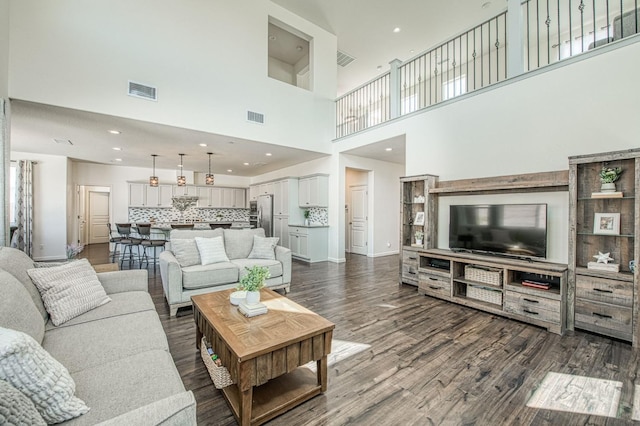 living room featuring a towering ceiling, visible vents, dark wood-style flooring, and baseboards
