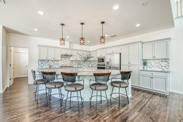 kitchen with tasteful backsplash, a spacious island, stainless steel appliances, visible vents, and dark wood-type flooring