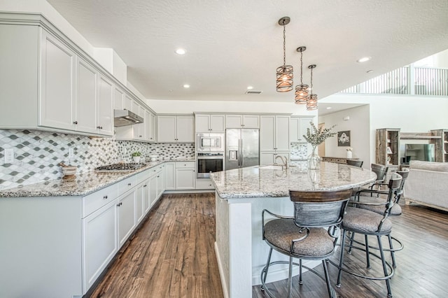 kitchen with a sink, dark wood-style flooring, stainless steel appliances, a breakfast bar area, and light stone counters