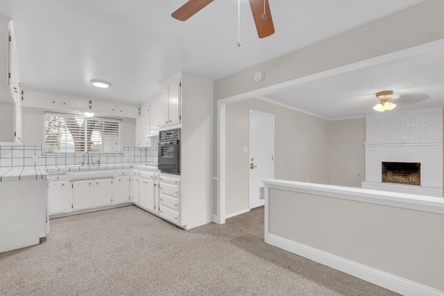 kitchen featuring black oven, a sink, light colored carpet, light countertops, and a ceiling fan