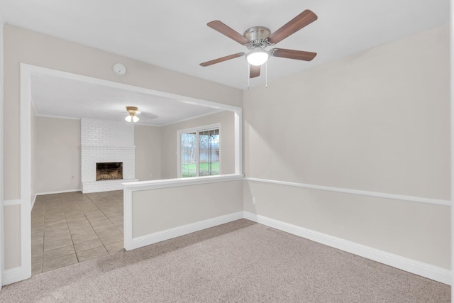 carpeted empty room with tile patterned flooring, a ceiling fan, baseboards, and a fireplace
