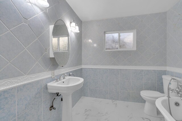 bathroom featuring a sink, toilet, marble finish floor, and tile walls