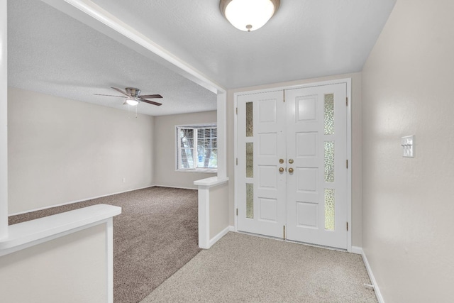 carpeted foyer entrance featuring a textured ceiling, ceiling fan, and baseboards