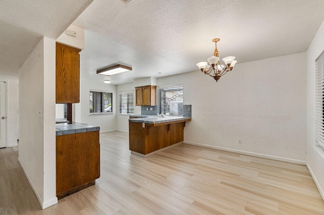 467 E Alluvial Ave Unit 106, Fresno, CA 93720 - kitchen featuring light wood-style floors, brown cabinetry, a chandelier, a peninsula, and a textured ceiling