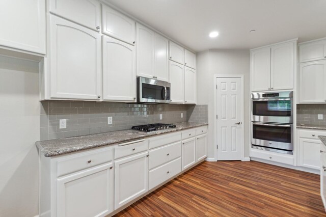 kitchen with dark wood-style flooring, white cabinets, backsplash, and stainless steel appliances