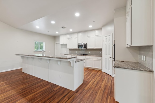 kitchen with stainless steel microwave, dark wood-style floors, visible vents, backsplash, and white cabinetry