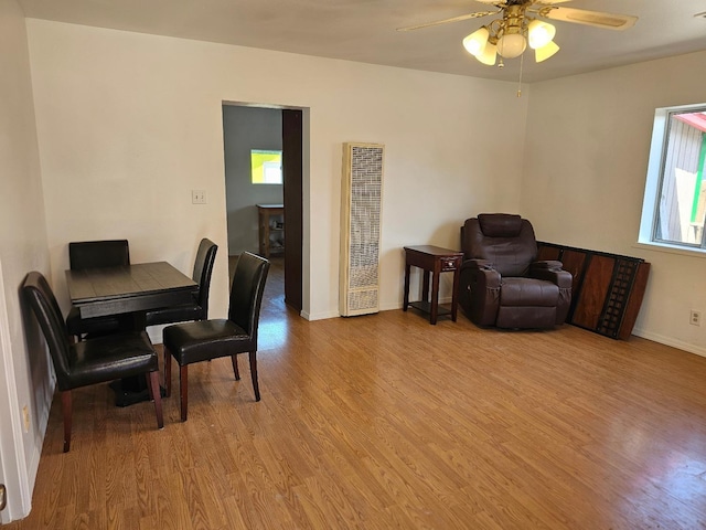 living area with a heating unit, a ceiling fan, light wood finished floors, and baseboards