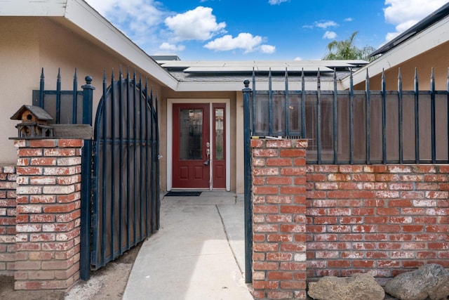 doorway to property featuring a gate, brick siding, fence, and roof mounted solar panels