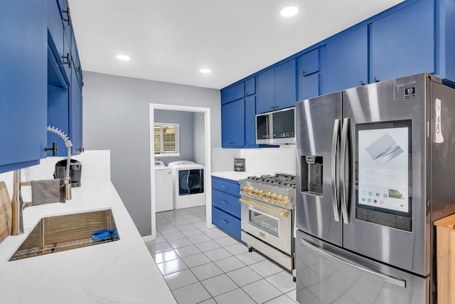 kitchen with blue cabinetry, appliances with stainless steel finishes, backsplash, a sink, and washing machine and dryer