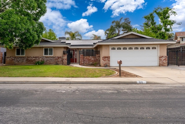ranch-style home featuring roof mounted solar panels, concrete driveway, an attached garage, brick siding, and a front lawn