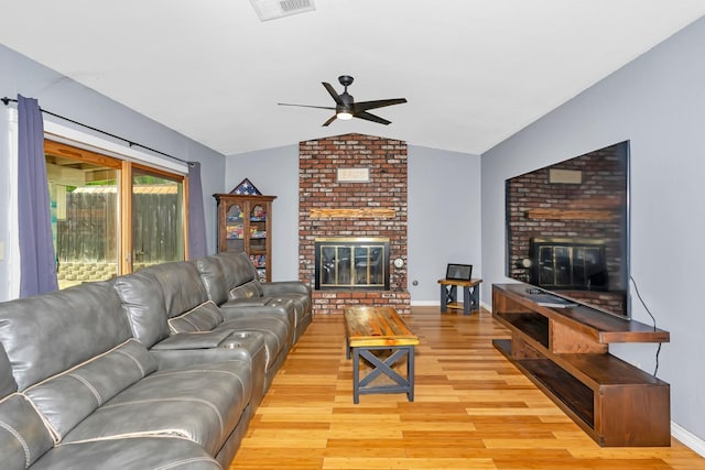 living area with wood finished floors, a ceiling fan, vaulted ceiling, and a brick fireplace