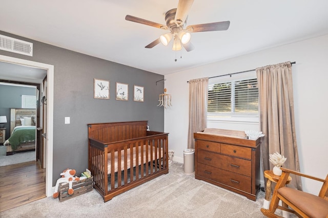 bedroom featuring ceiling fan, visible vents, light carpet, baseboards, and a crib