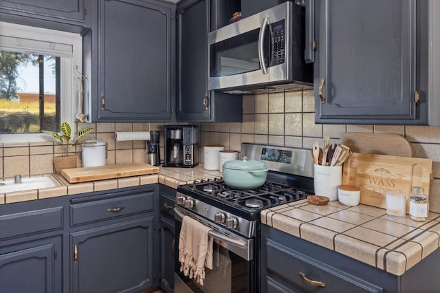kitchen with blue cabinets, tile countertops, appliances with stainless steel finishes, and backsplash