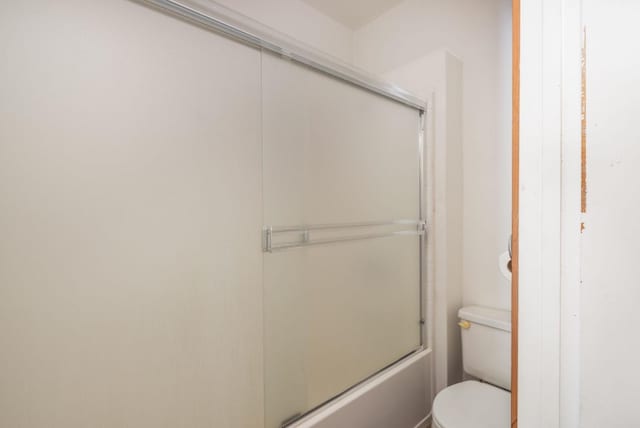 bathroom featuring toilet and bath / shower combo with glass door